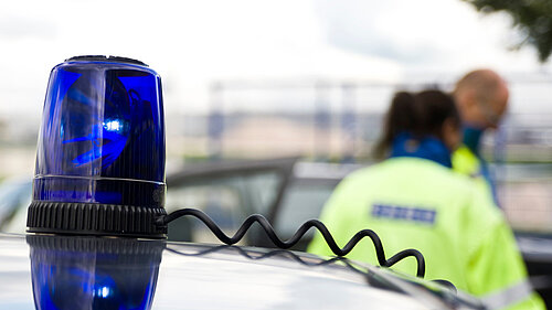 Police officers in the background, with a blue light on a vehicle in the foreground 